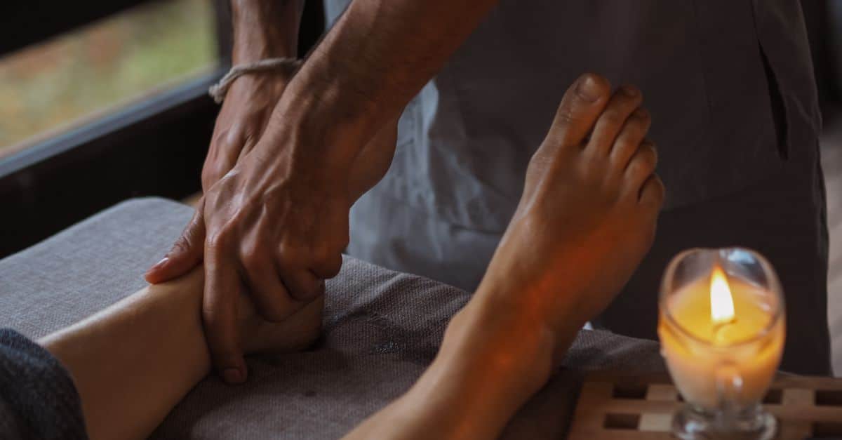 Close-up of a soothing foot massage in a dimly lit spa setting with a candle.